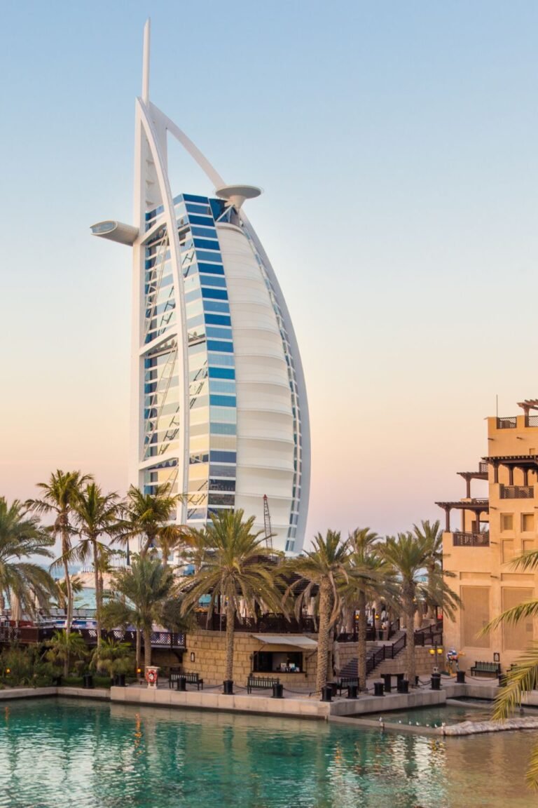 Burj Al Arab hotel towering over palm trees and waterfront, symbolizing luxury travel experiences in Dubai, UAE.